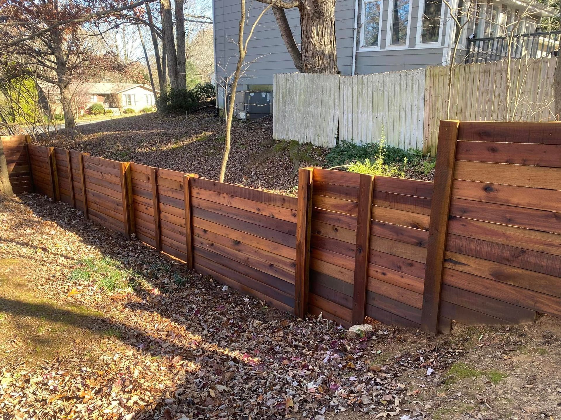 A wooden fence is surrounded by leaves in front of a house.