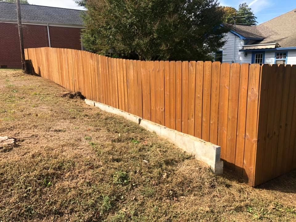 A wooden fence is sitting in the middle of a grassy field in front of a house.