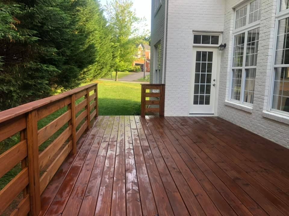 A large wooden deck with a wooden railing in front of a white brick house.
