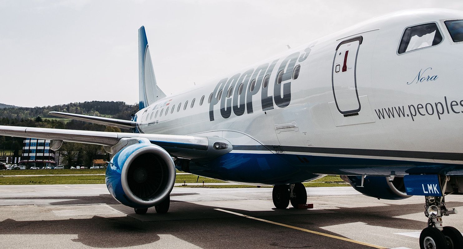 Flugzeug der Airline People’s am Boden auf dem Rollfeld, seitlich fotografiert mit sichtbarem Triebwerk und Logo.