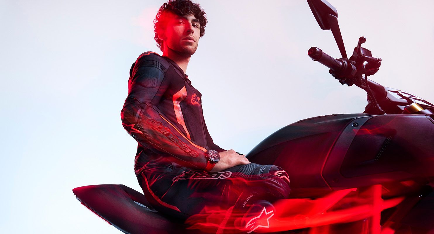 Motorradrennfahrer Enea Bastianini in Lederkombi auf einem Motorrad, inszeniert mit rotem Licht und sportlicher Pose.