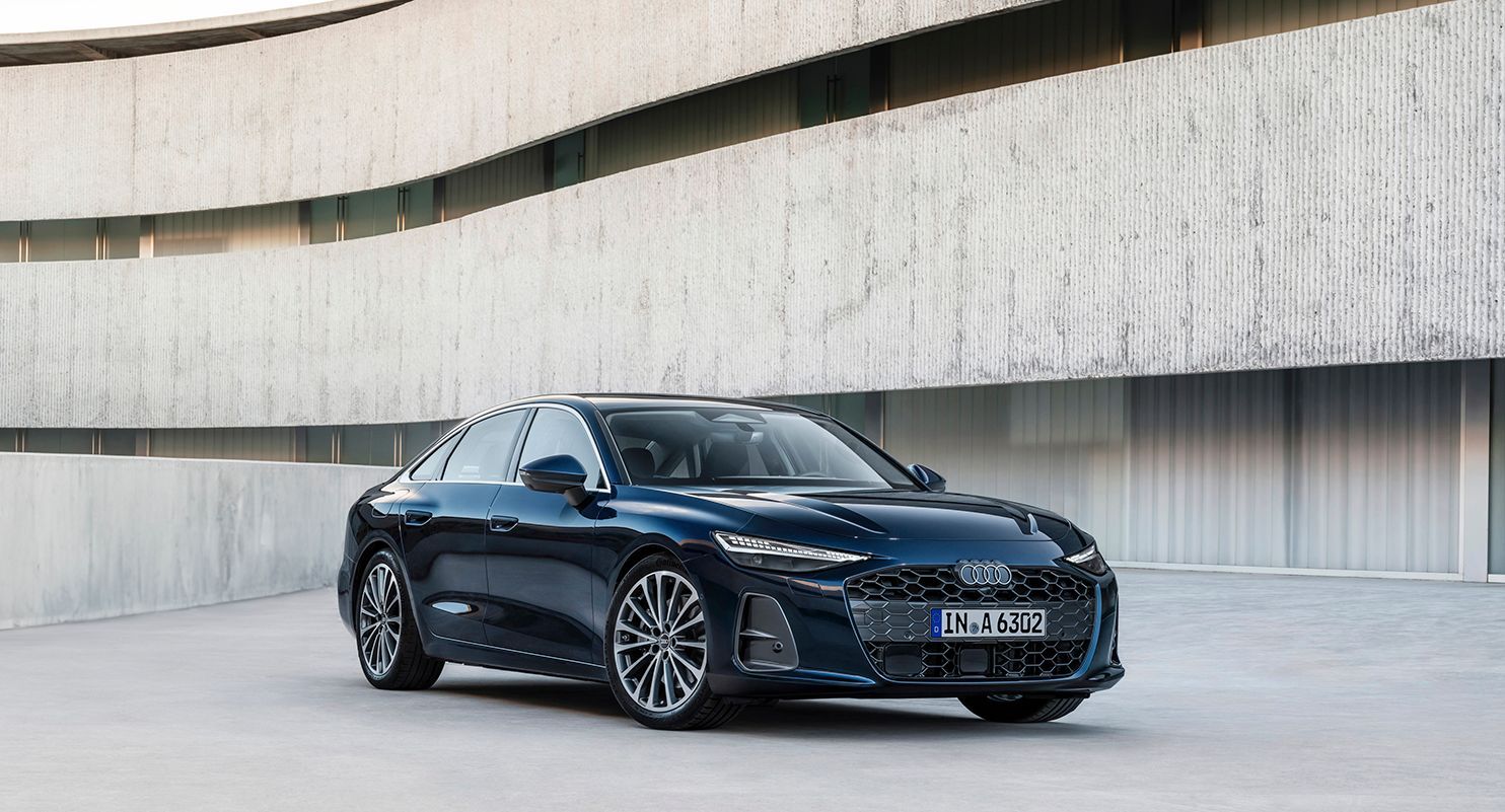 Dunkelblauer Audi A6 vor moderner Betonfassade, fotografiert im Stand aus schräger Frontansicht.