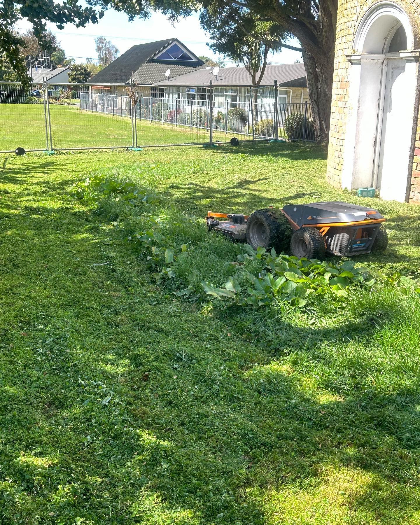 Robotic lawnmower on grassy yard, near a building.
