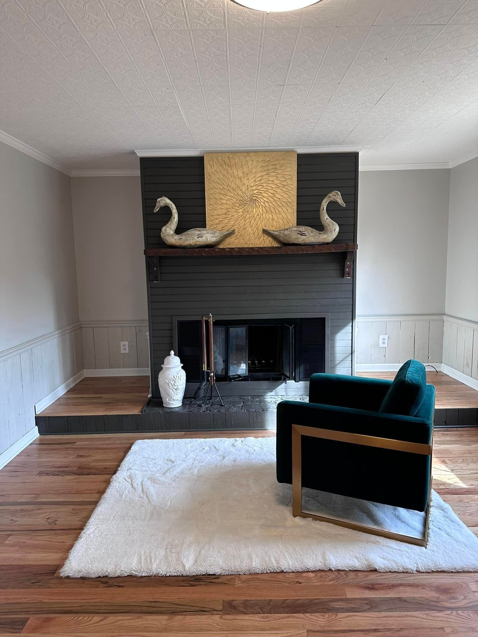 Fireplace with decorative swans, gold accents, green armchair, and white rug in a living room.