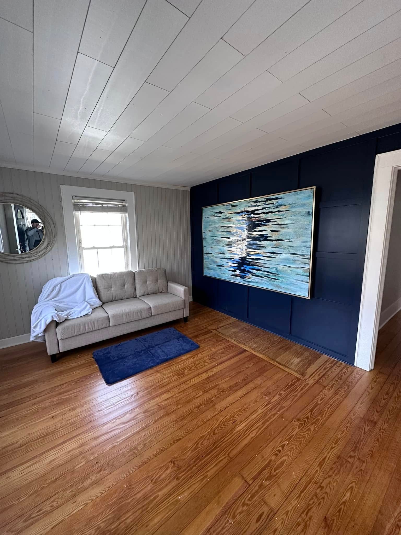 Living room with blue accent wall, sofa, artwork, and hardwood floors.