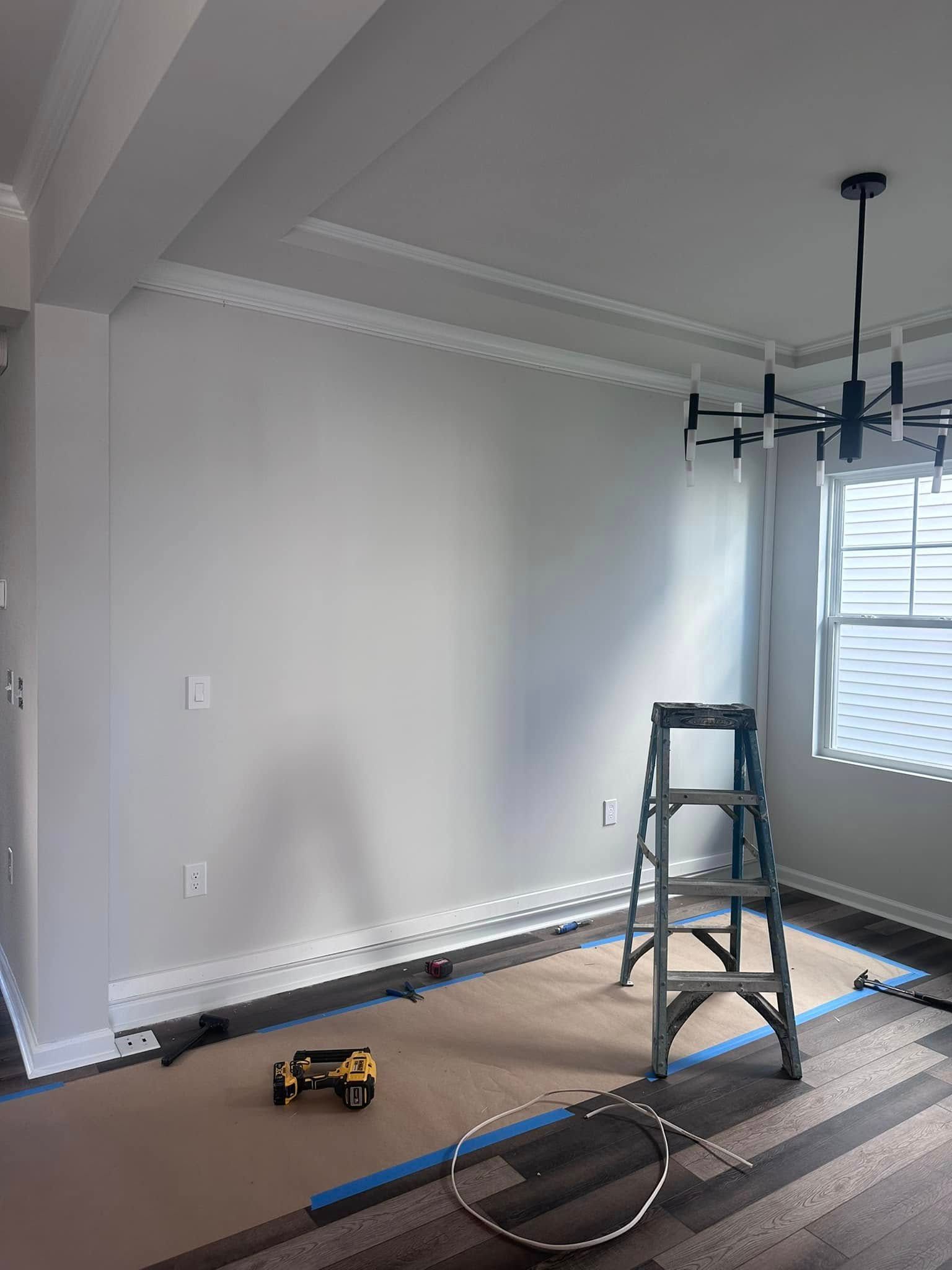 Room with ladder, tools, and crown molding under construction, with a window and a modern chandelier.