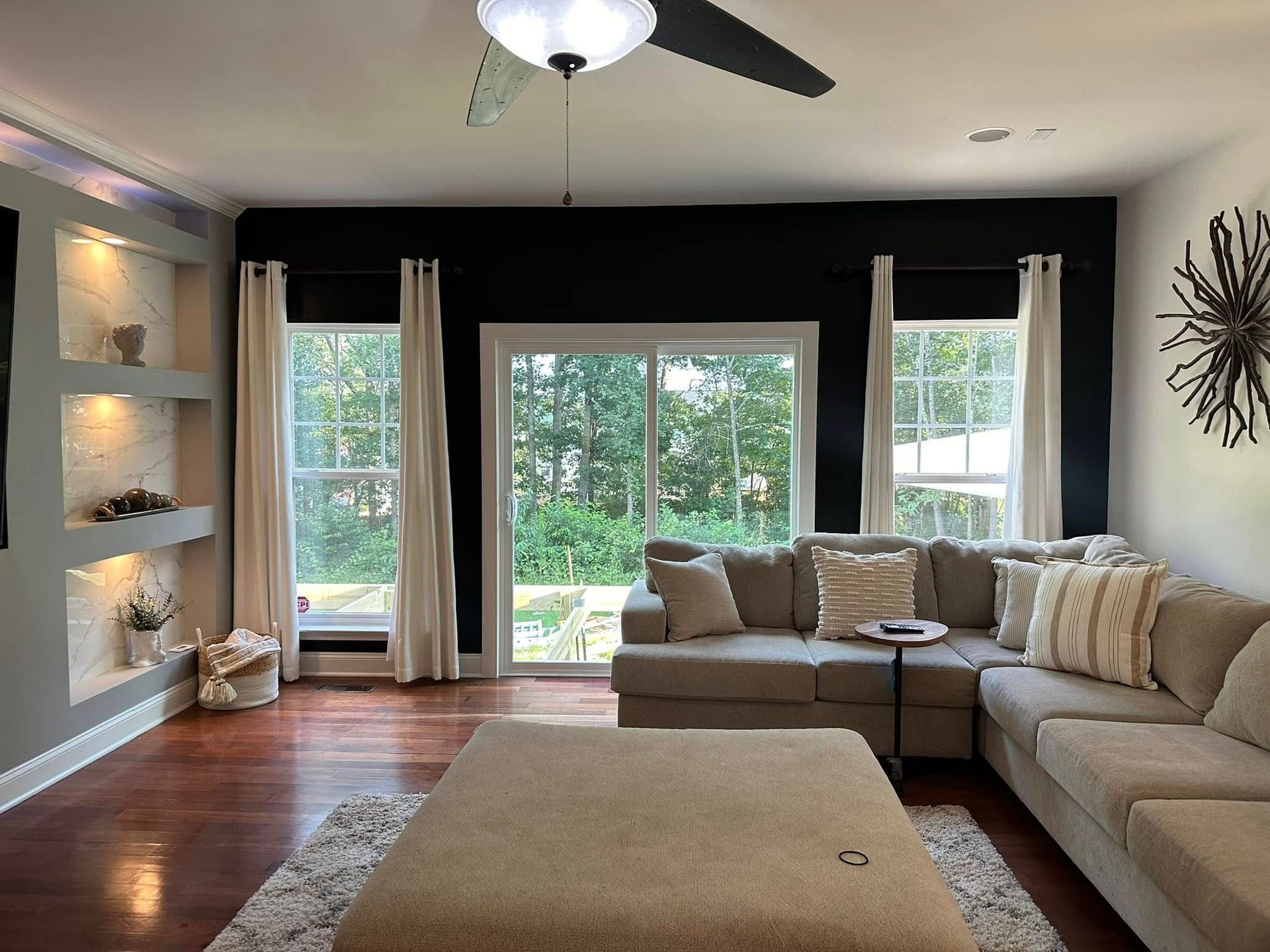 Living room with dark accent wall, sectional sofa, windows, and built-in shelves.