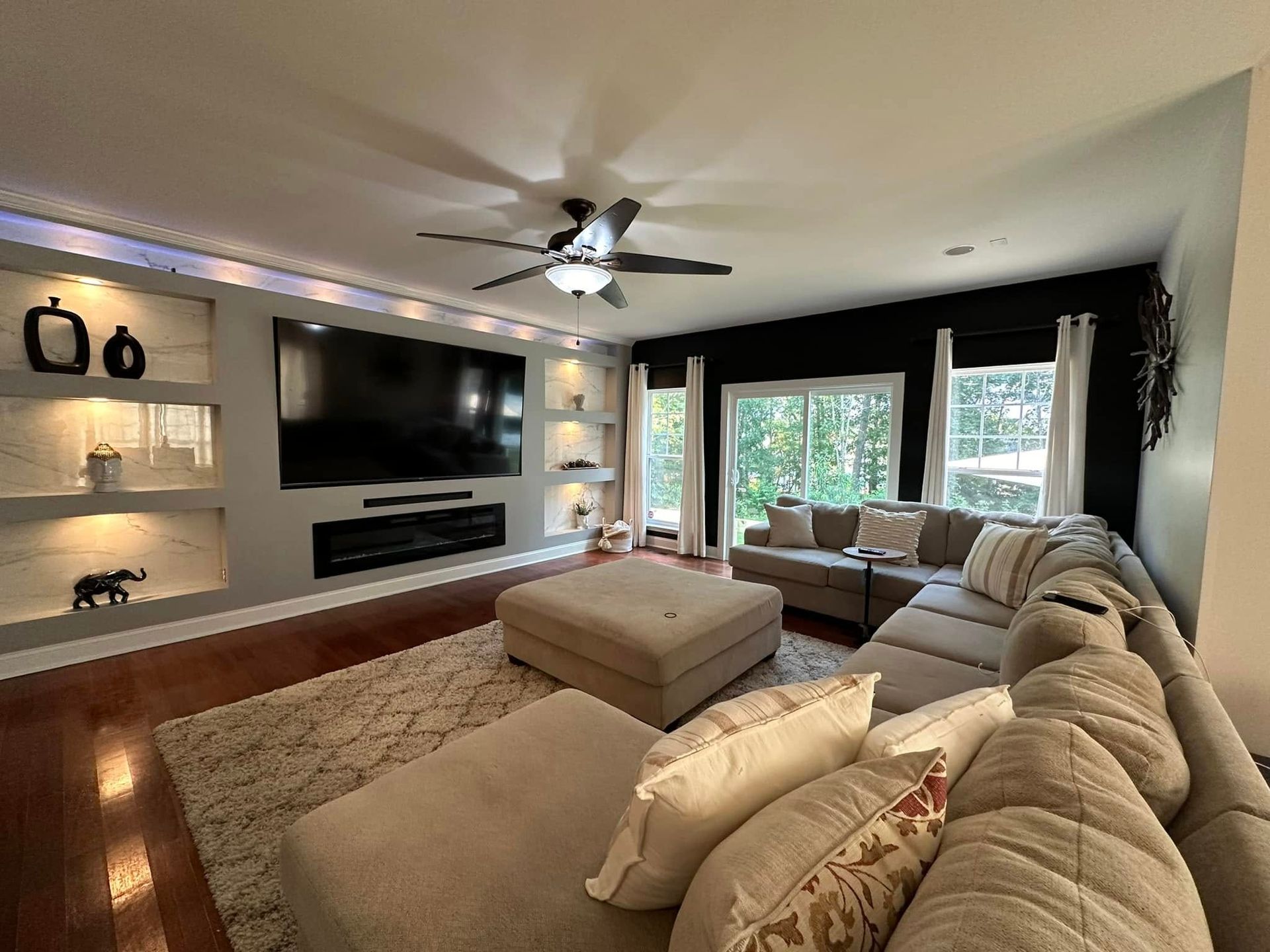 Living room with a large TV, sectional sofa, and built-in shelving with recessed lighting.