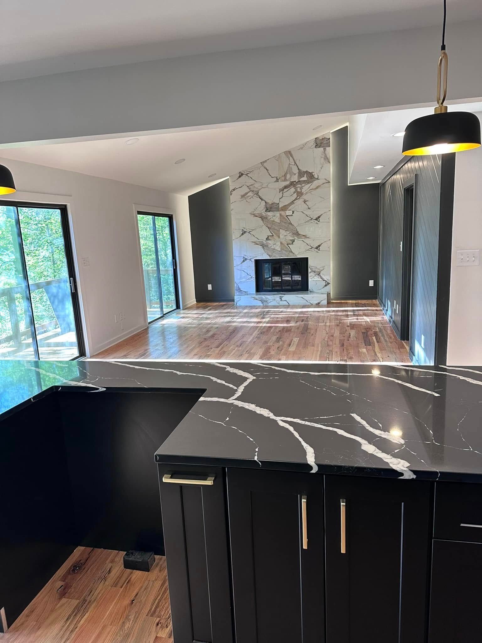 Modern kitchen and living space, black cabinets with gold hardware, marble countertops. Fireplace with marble accent wall.
