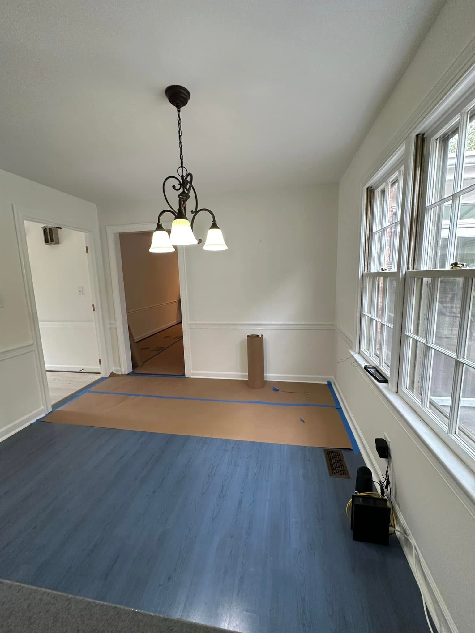 Dining room with blue floor, white walls, and a chandelier. A cardboard-covered doorway is visible.