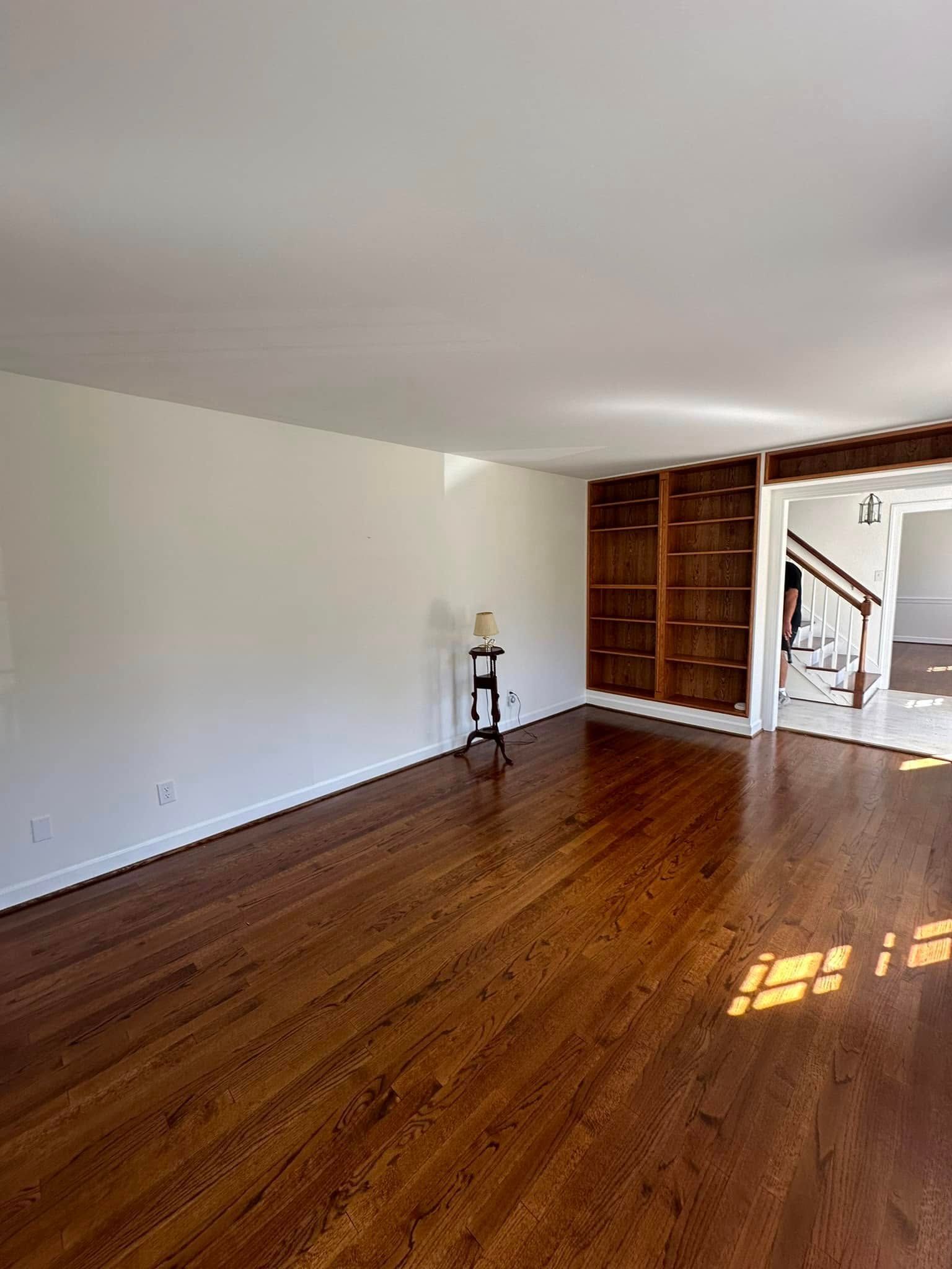 Empty living room with wood floors, white walls, and built-in wooden shelving.