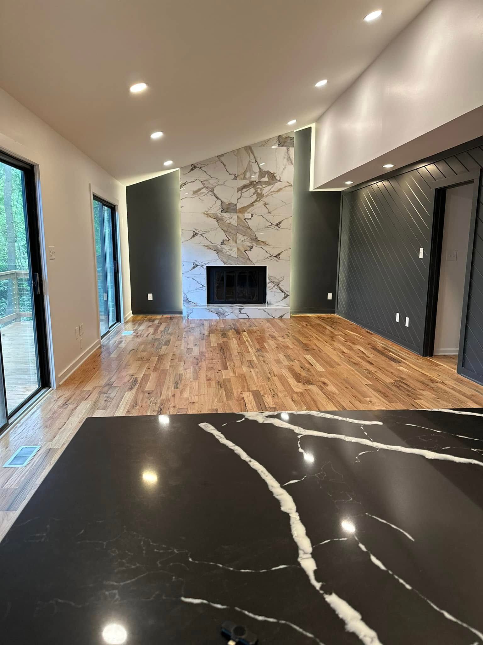 Spacious living room with hardwood floors, marble fireplace, and angled ceiling. Kitchen island in foreground.