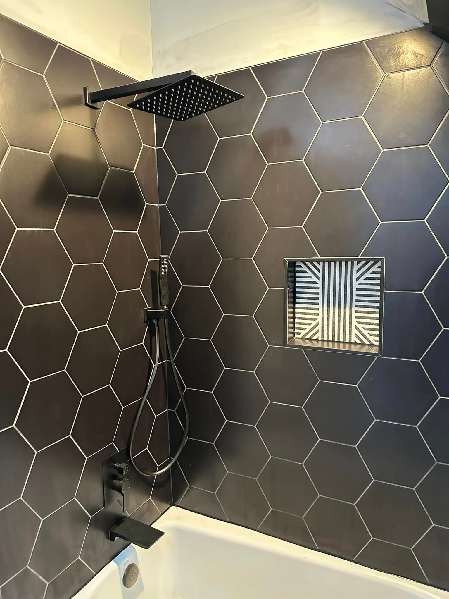 Black hexagonal tile shower with black fixtures and built-in shelf.