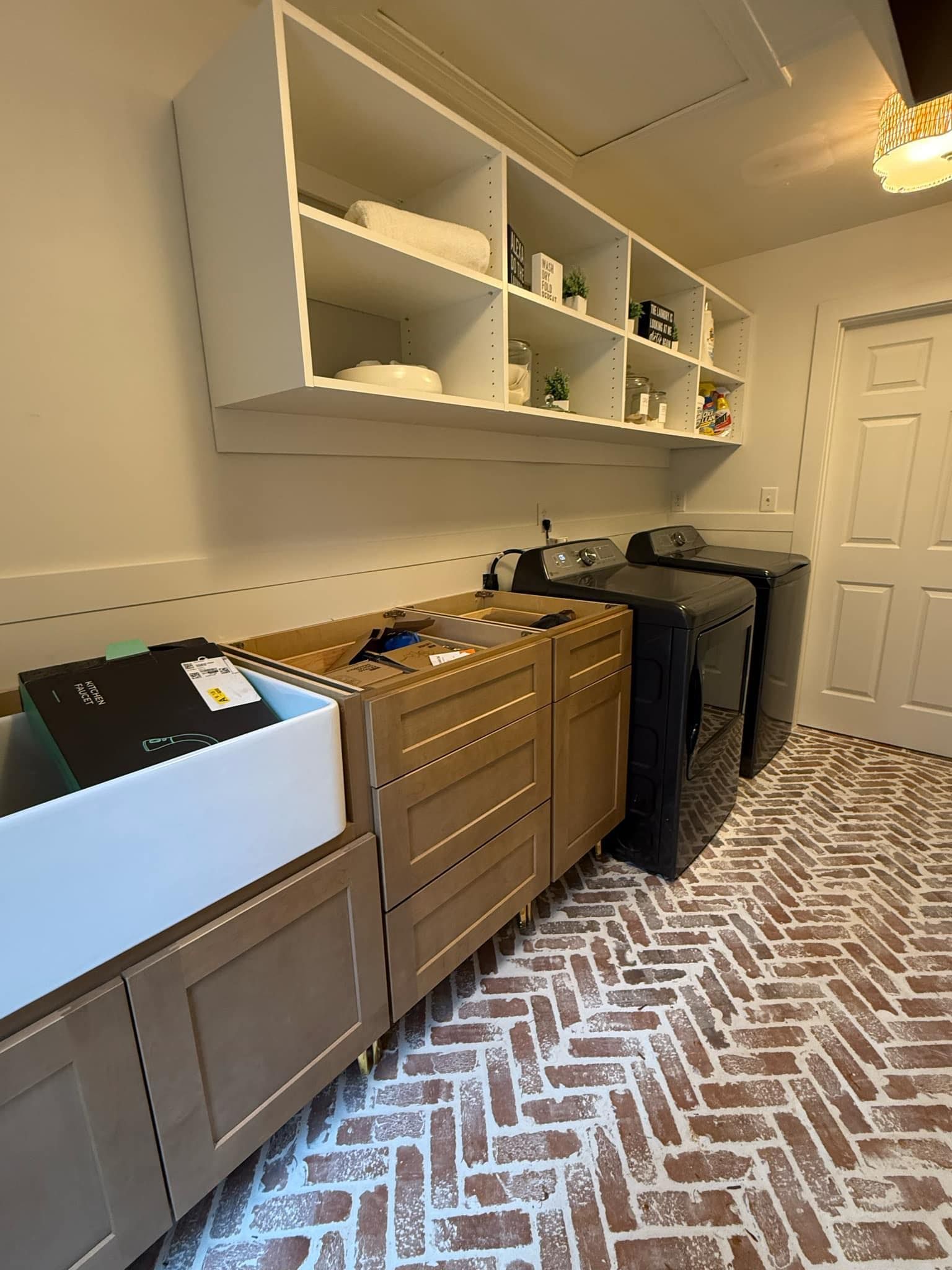Laundry room with brick-patterned floor, white cabinets, and shelves above the machines.