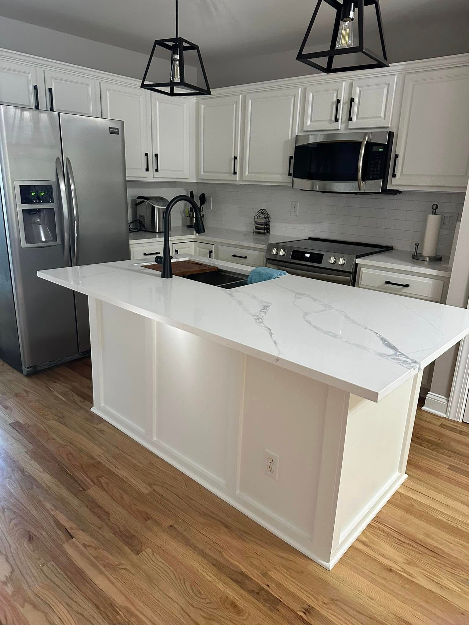 White kitchen with an island, hardwood floors, stainless steel appliances, and black light fixtures.