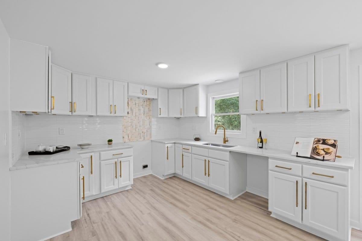 White kitchen with gold hardware, subway tile backsplash, and light wood flooring.