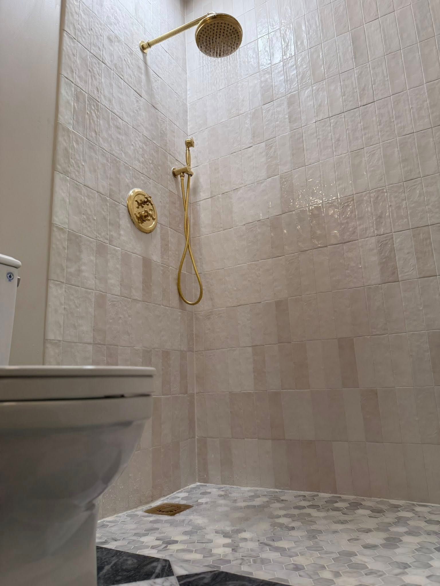 Gold shower fixtures and textured tile in a bathroom. A toilet is in the foreground.