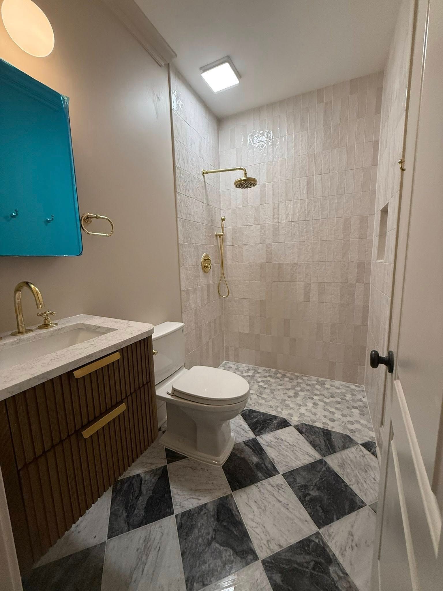 Bathroom with patterned floor, shower, toilet, wooden vanity, and gold fixtures.