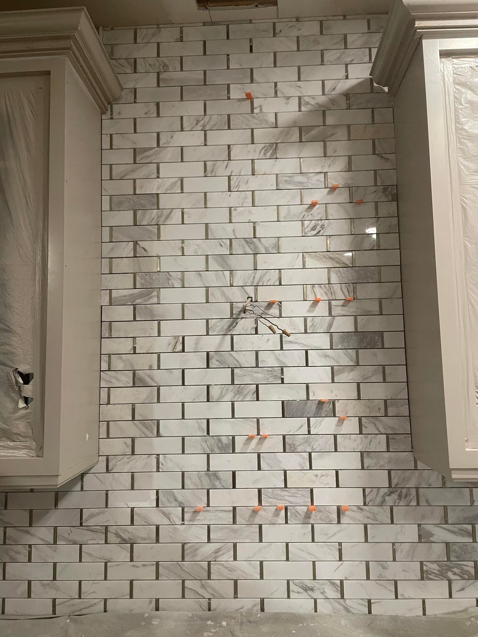 Close-up of a kitchen backsplash partially covered with white brick-patterned tiles, positioned between cabinets.
