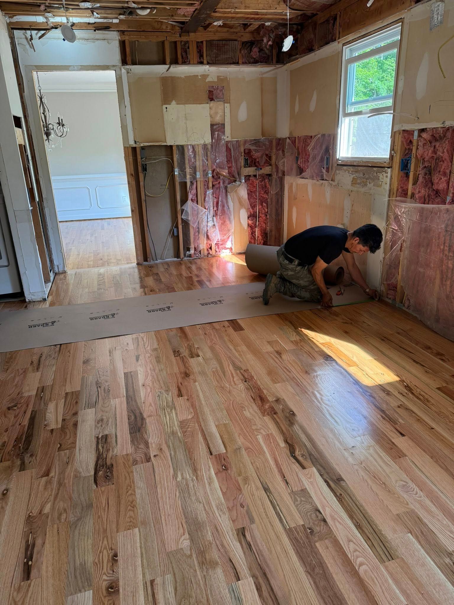 Person installing hardwood floor in room with exposed walls.