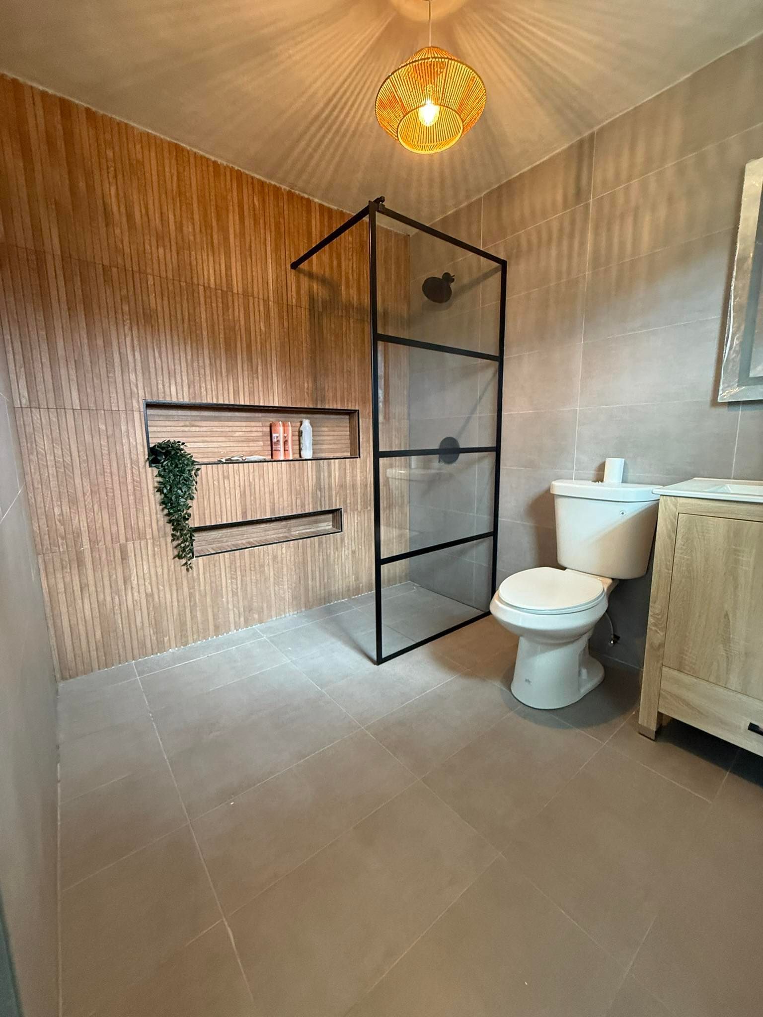 Bathroom with a glass shower, toilet, and wooden-look wall with a shelf.