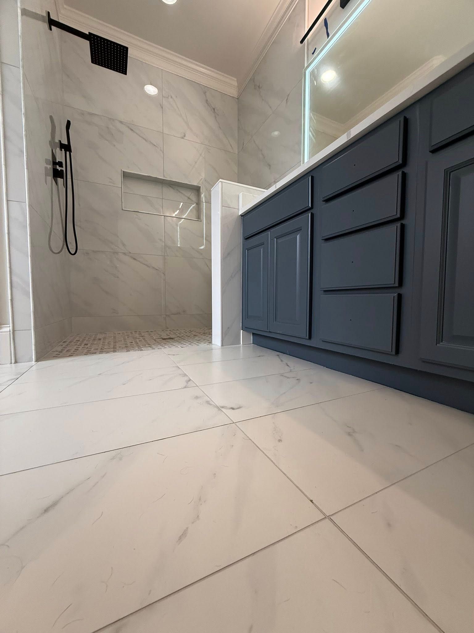 Bathroom with blue vanity, marble tile floor, and a glass-enclosed shower.