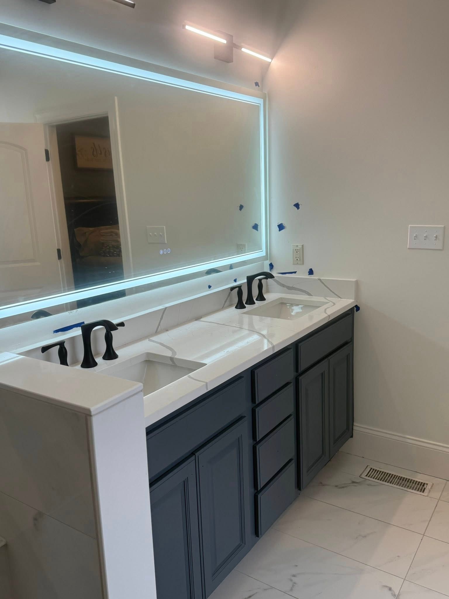 Bathroom with gray vanity, marble countertop, black fixtures, and large illuminated mirror.