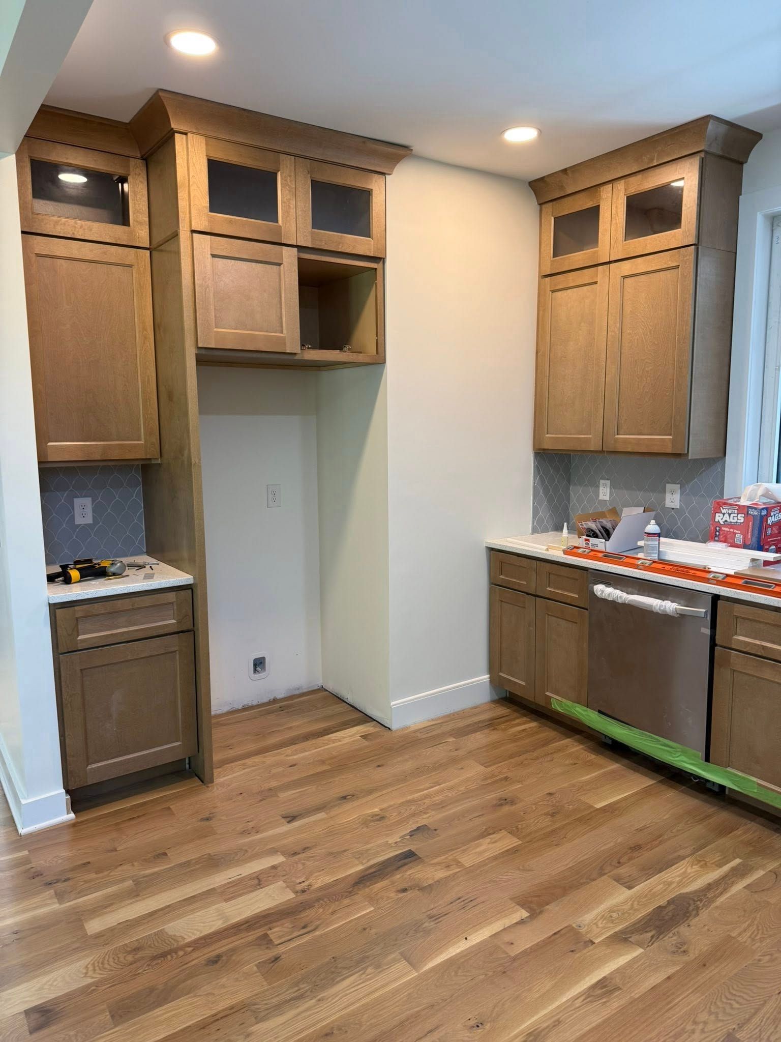 Kitchen under construction, wood cabinets, stainless steel appliances, light wood floors, empty refrigerator space.