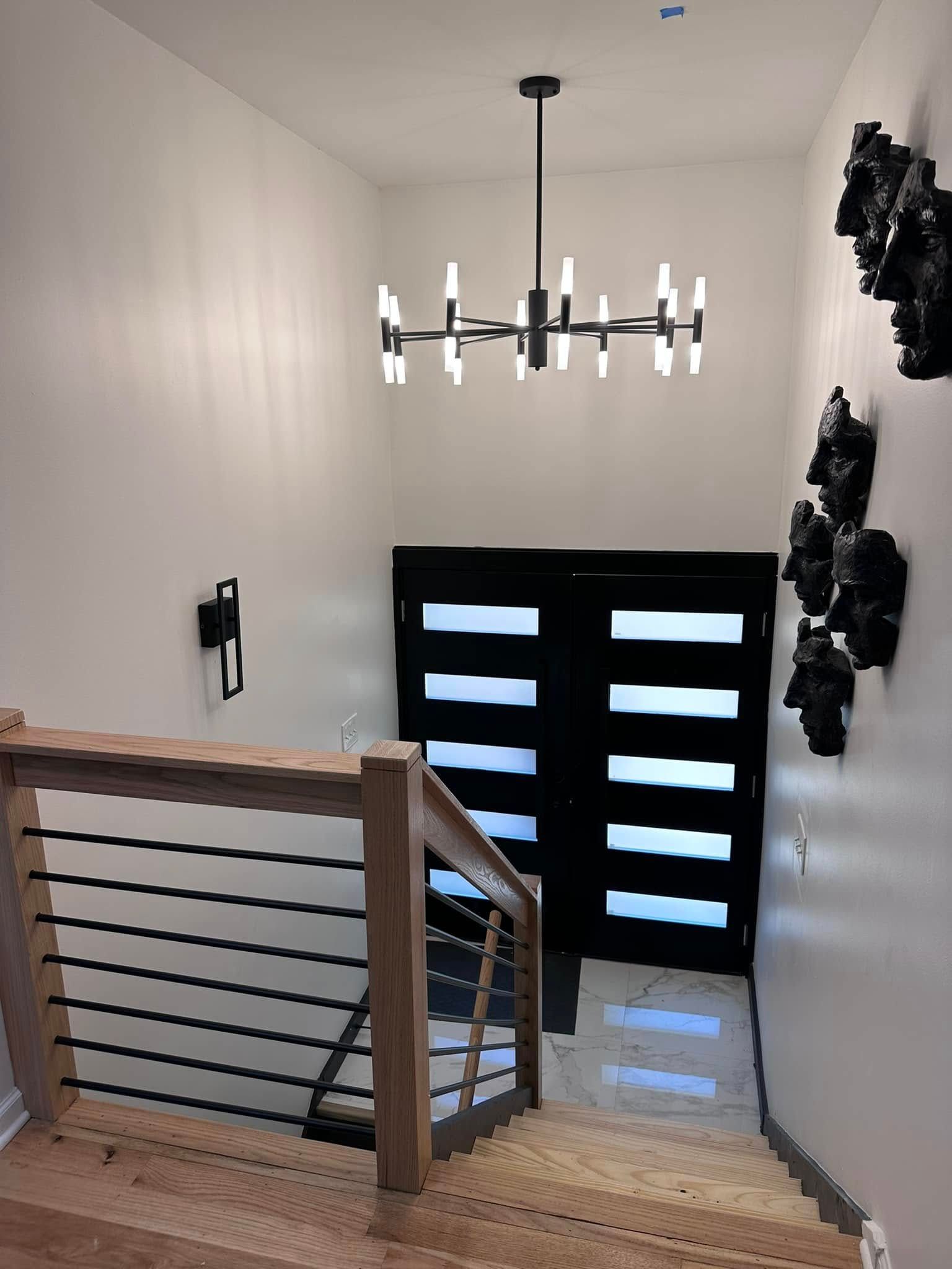 Entryway with stairs, modern chandelier, black front door, and abstract wall art. Wooden railing.