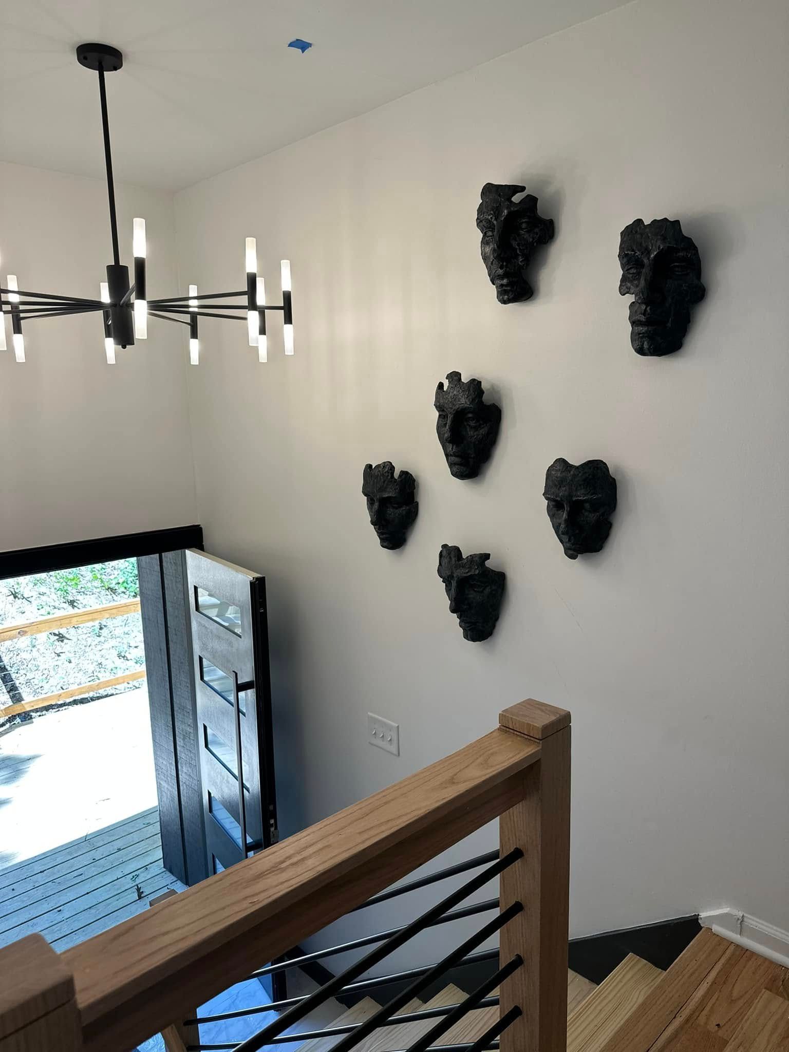 Stairwell with black art masks on white wall, chandelier, open black door, wood railing, and stairs.