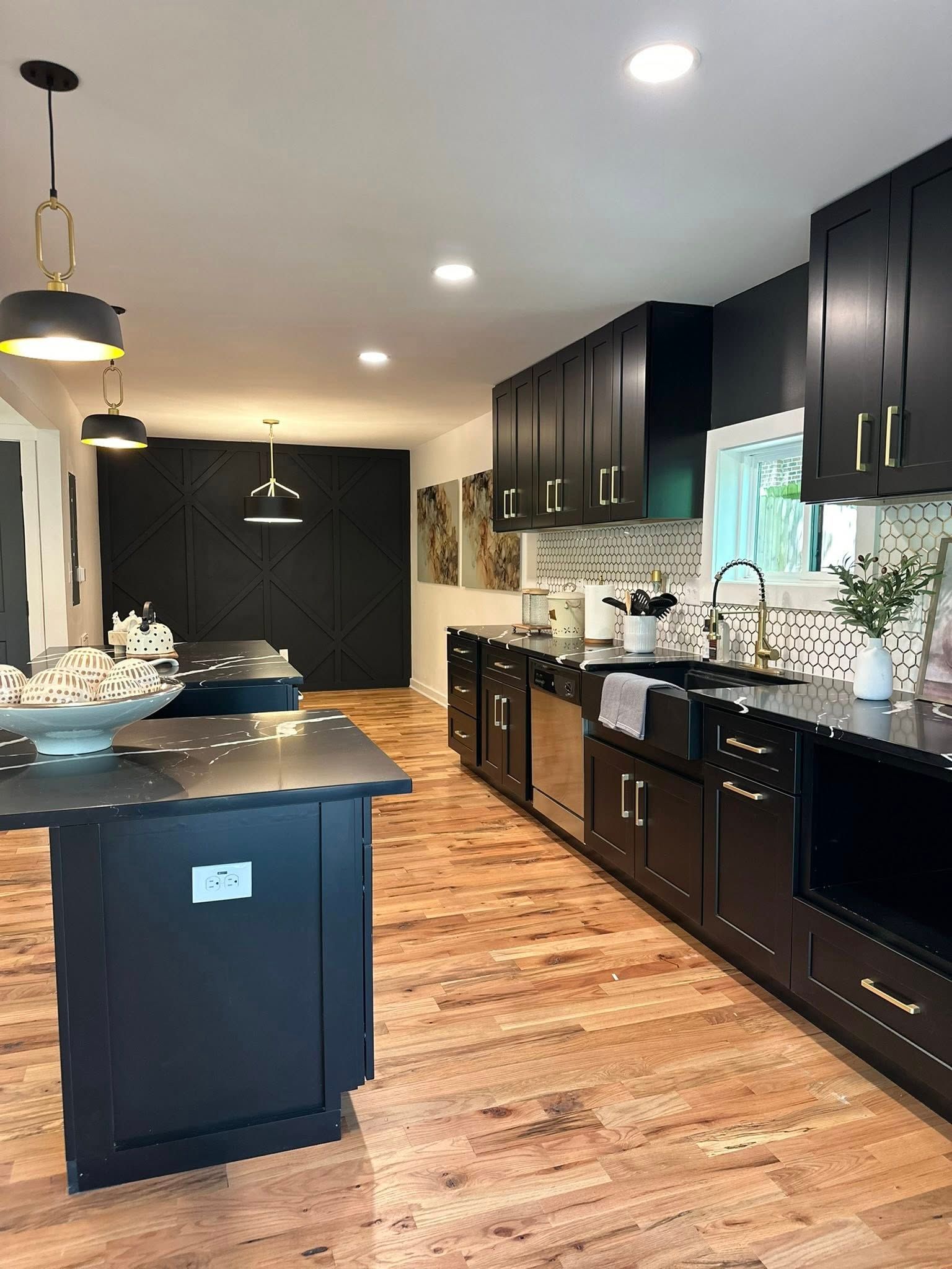 Black kitchen with wood floors, island, cabinets, and modern light fixtures.