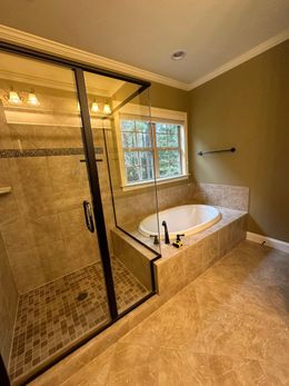 Bathroom with shower, tub, and window. Beige tile, dark shower frame, olive walls.