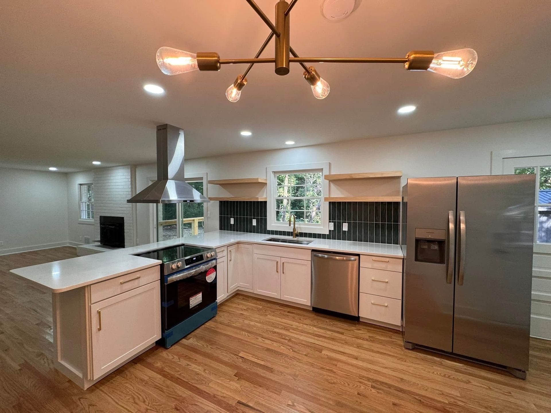 Modern kitchen with white cabinets, stainless steel appliances, wood floors, and a dark tile backsplash.