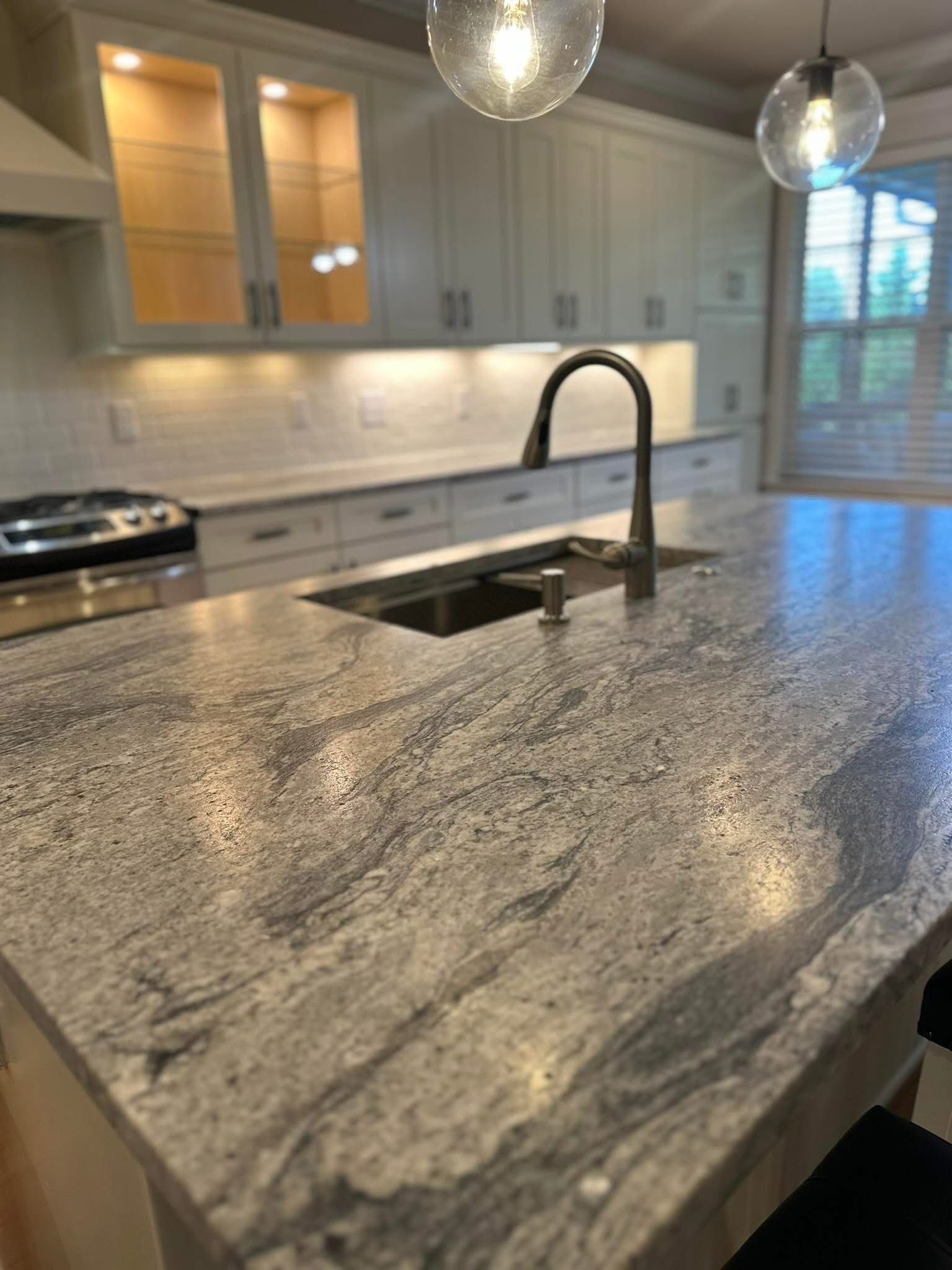 Kitchen with granite countertop island, stainless steel sink, and modern pendant lights.