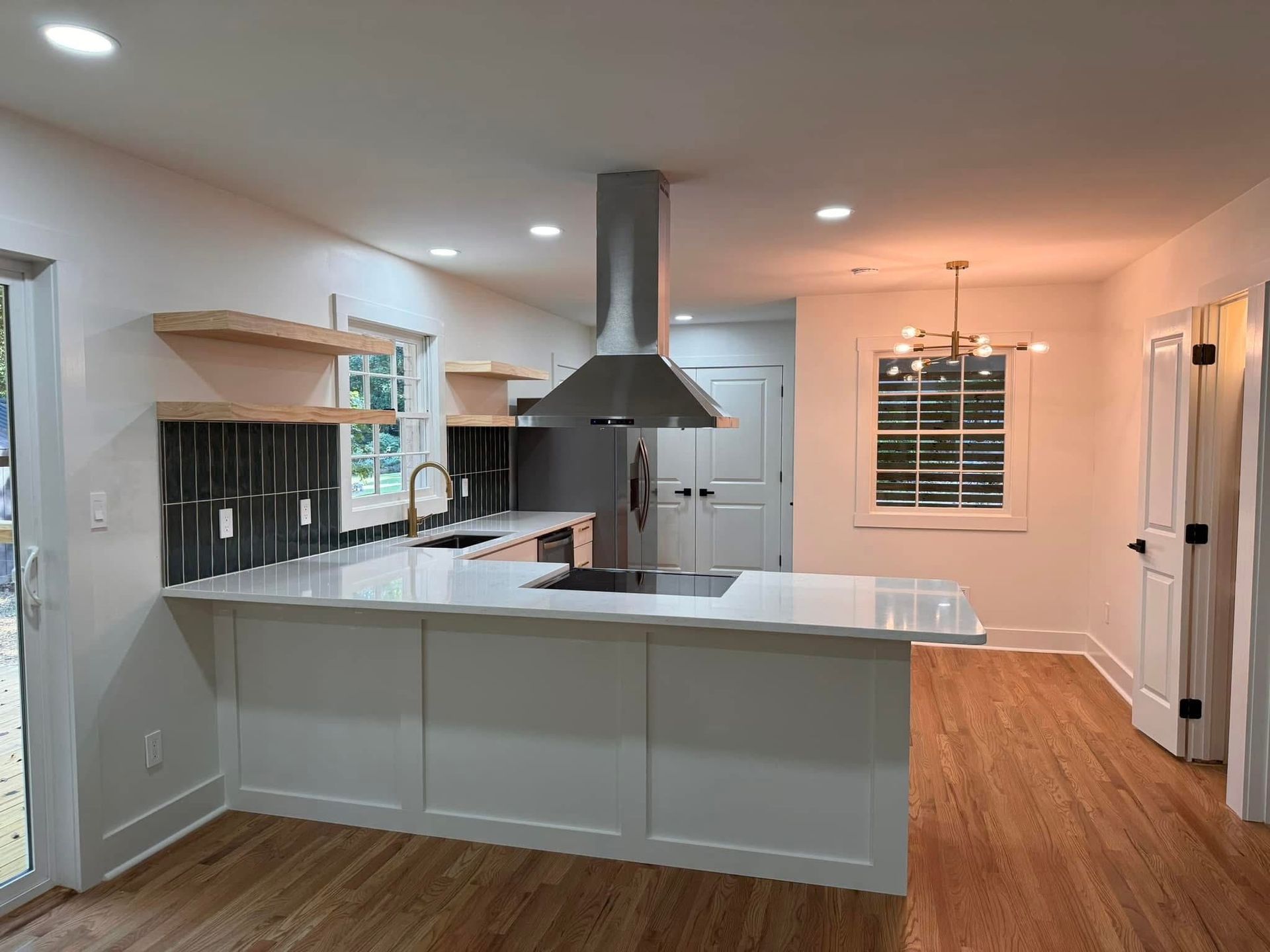 Modern kitchen with white island, stainless range hood, and wooden floors.