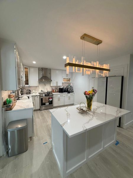 Modern white kitchen with island, quartz countertop, and gold chandelier.