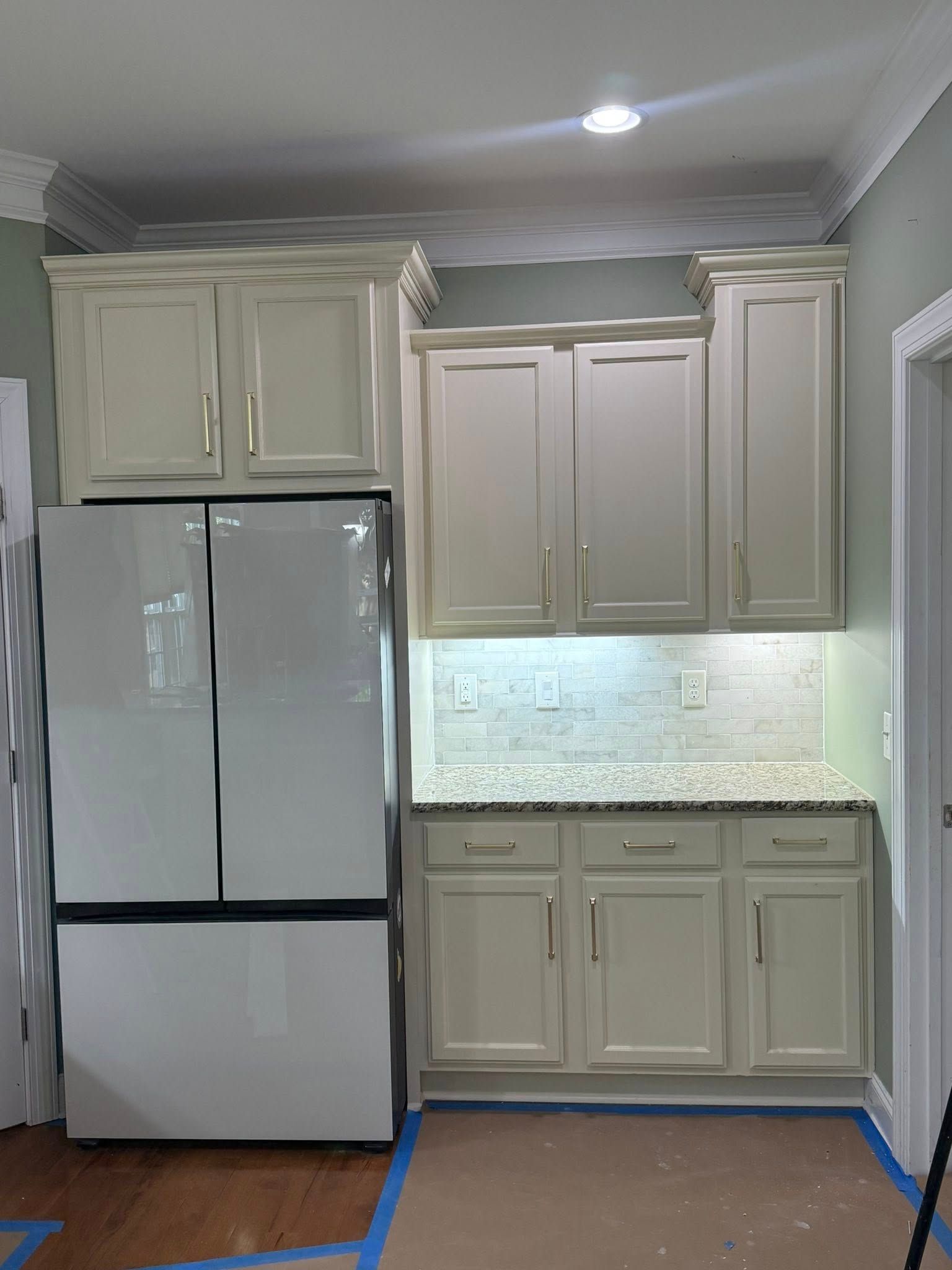 Cream-colored kitchen cabinets and refrigerator; white tile backsplash; granite countertop.