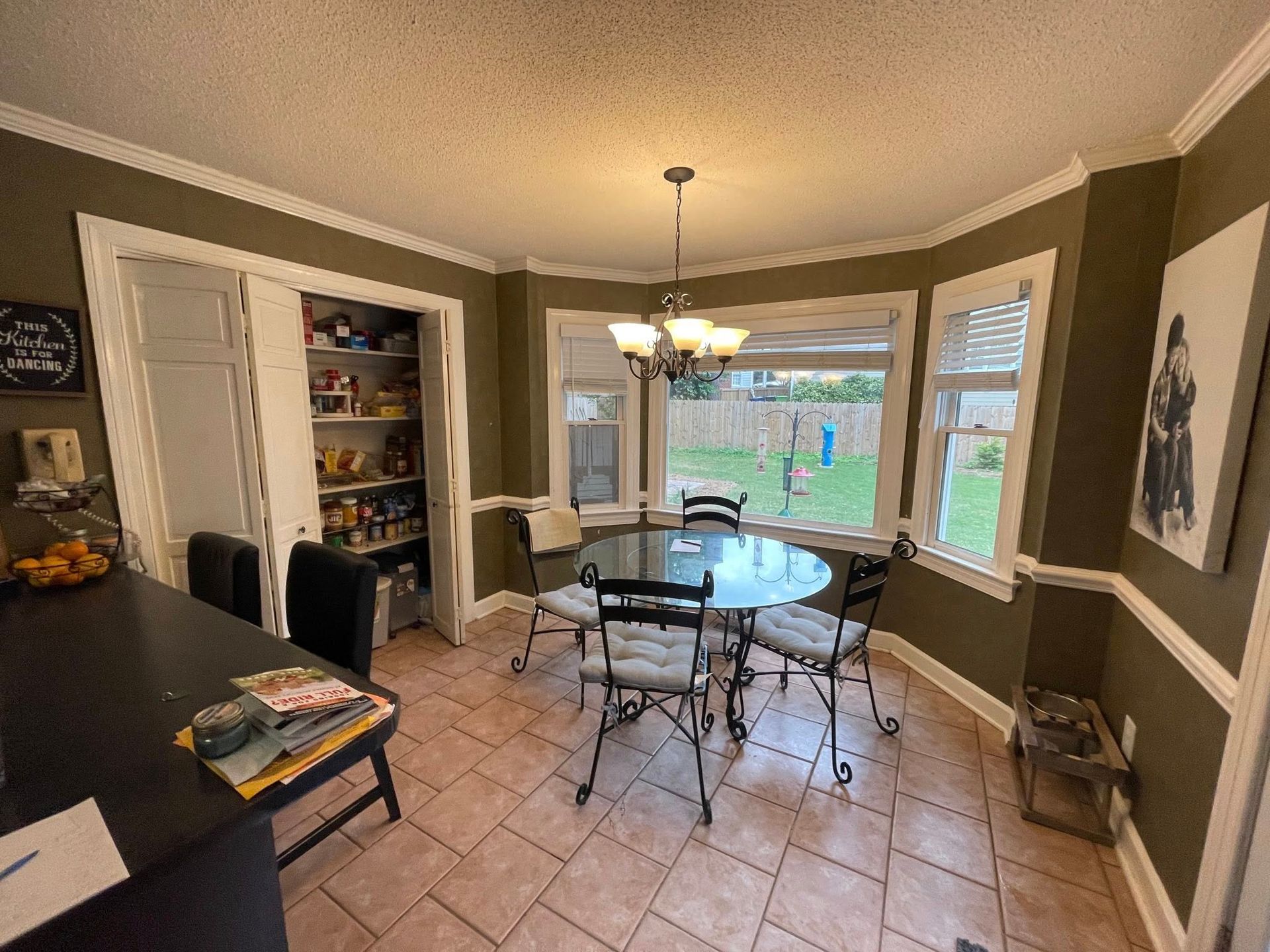 Dining room with round table, chairs, pantry, and windows overlooking a yard.