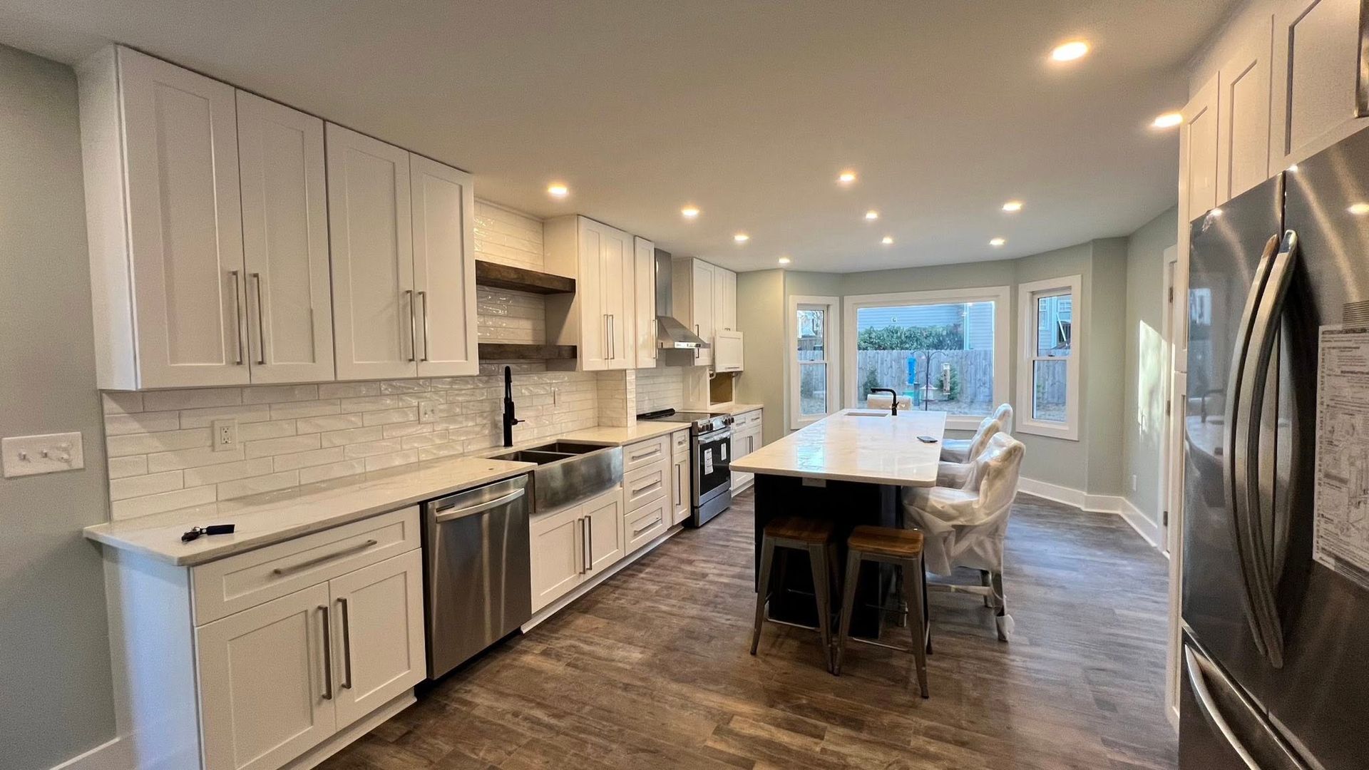 Modern white kitchen with island, stainless steel appliances, and wooden floor.
