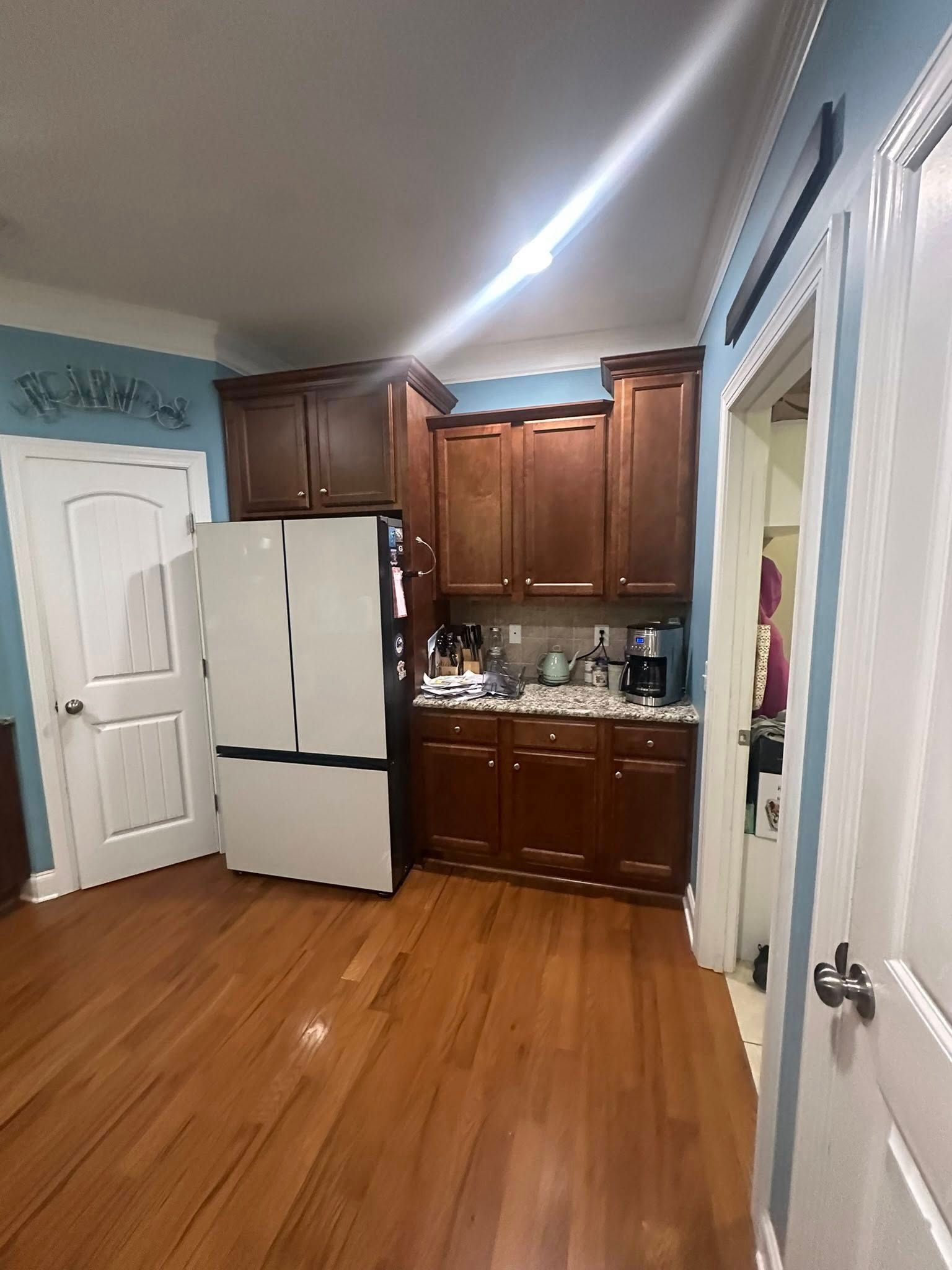 Kitchen with wood cabinets, white refrigerator, hardwood floor, and a white door.
