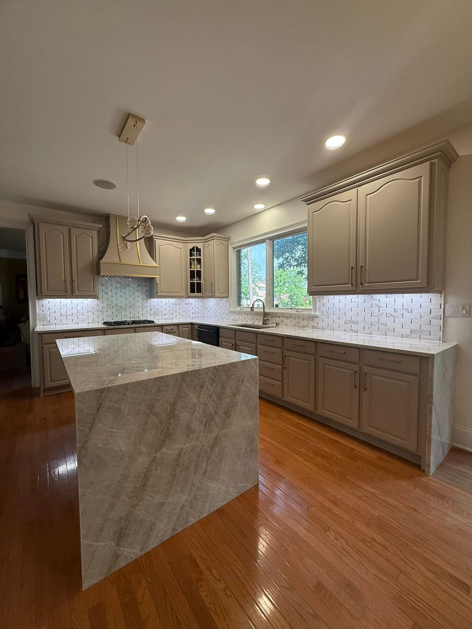 A kitchen with light grey cabinets, marble countertops, and a large island.