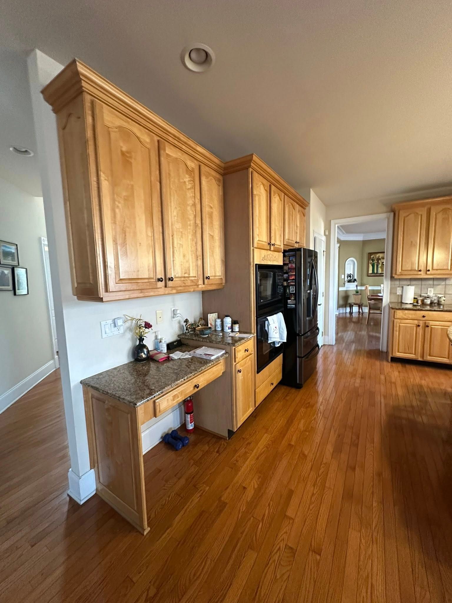 Kitchen with wooden cabinets and a built-in desk. Black oven and refrigerator. Hardwood floors.