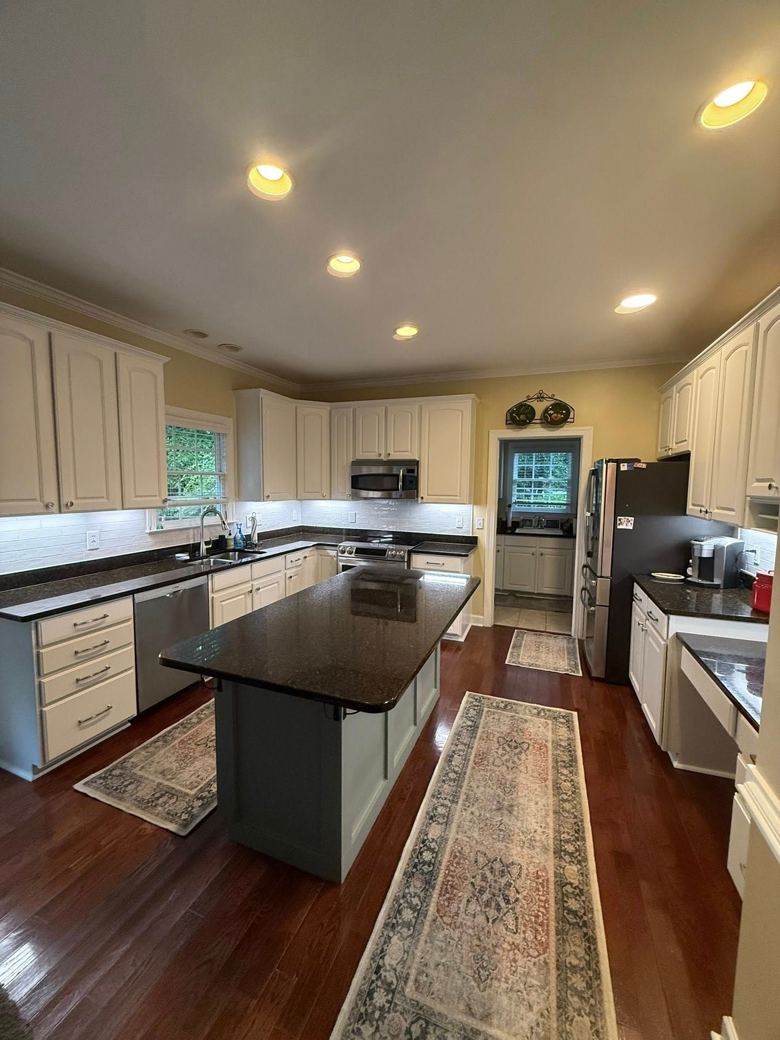 Kitchen with white cabinets, dark countertops, a gray island, and two rugs on hardwood flooring.