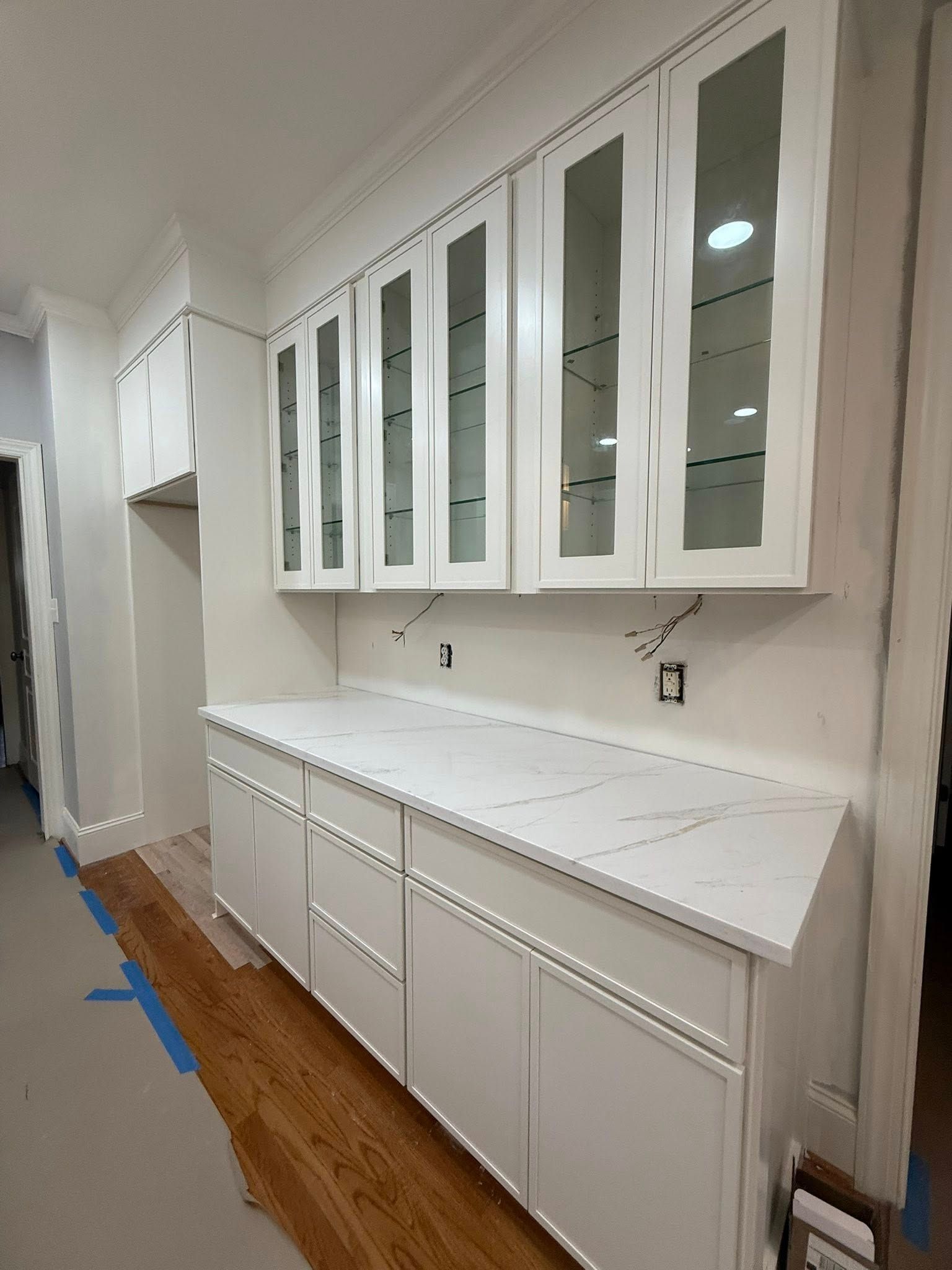 White kitchen cabinets with glass doors, white countertops, and wood flooring.