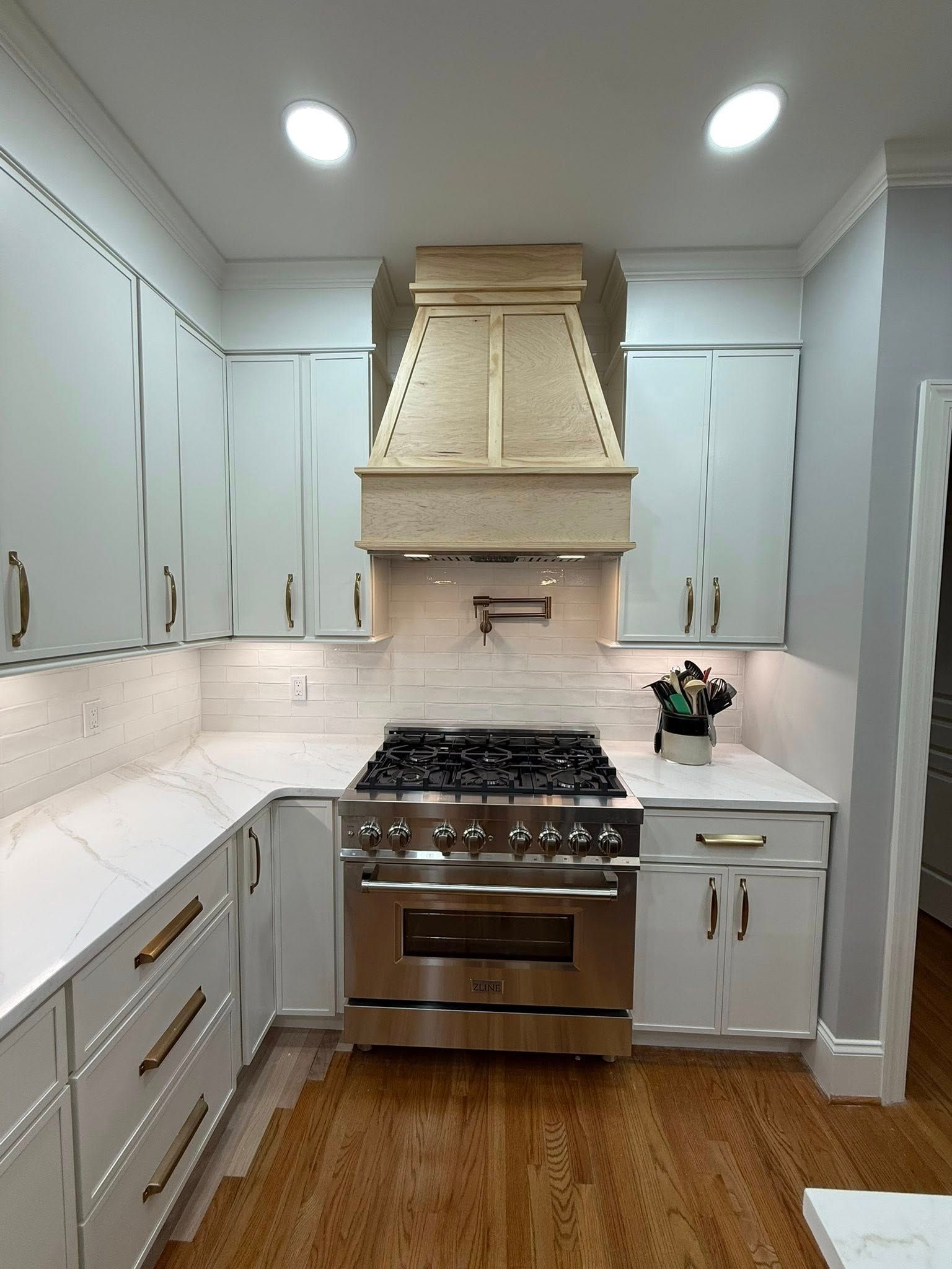 White kitchen with stove, range hood, cabinets, countertops, and hardwood floors.