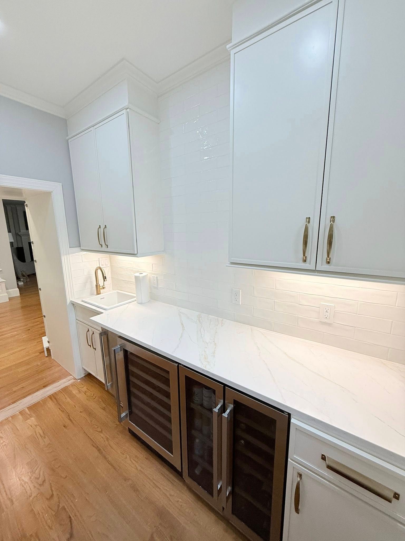 White kitchen cabinets and countertops with a built-in wine cooler and under-cabinet lighting.