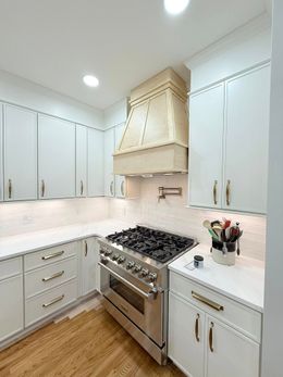 White kitchen with stainless steel stove and range hood. Cabinets, countertops, and wood floor.