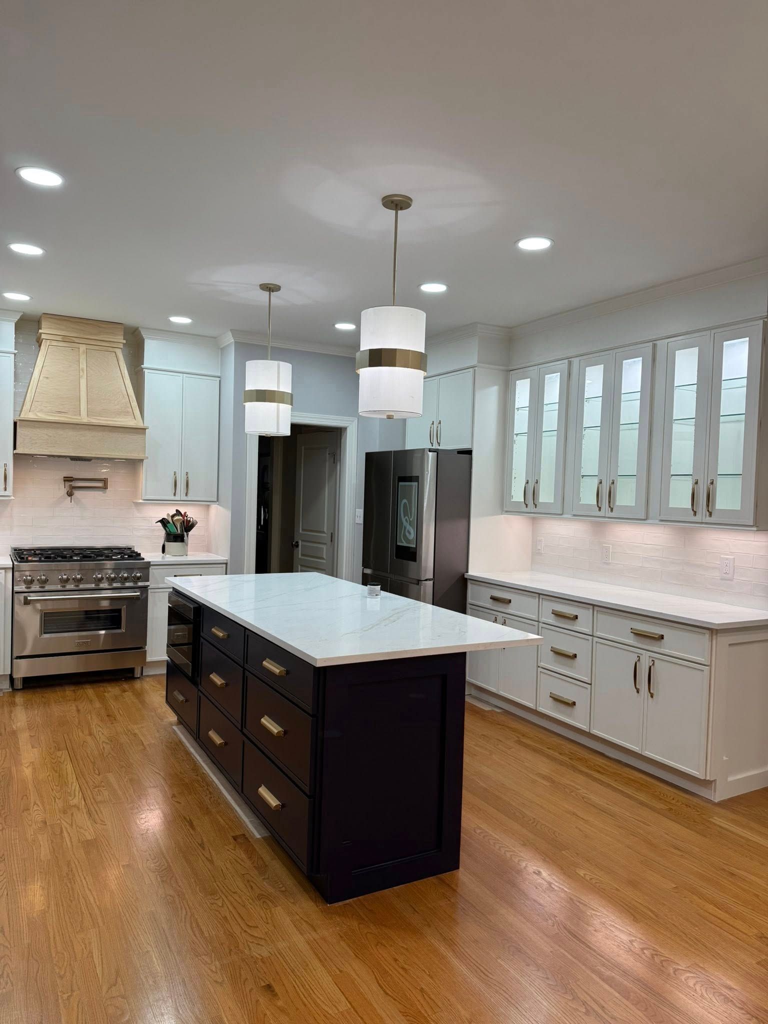 Kitchen with hardwood floors, light blue cabinets, dark island with white countertop, stainless steel appliances, and pendant lights.