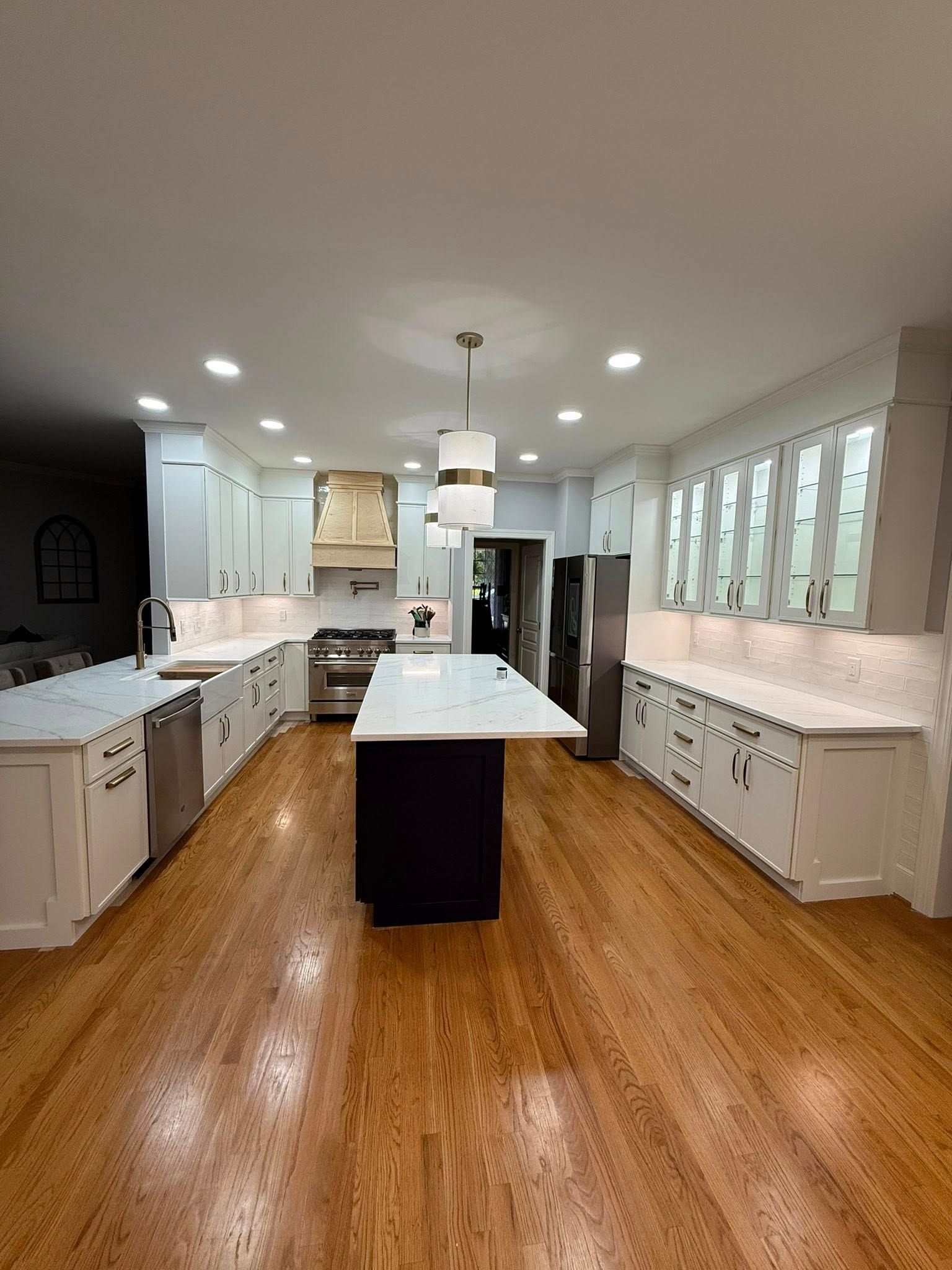 Modern white kitchen with dark island and wood floors, under-cabinet lighting.
