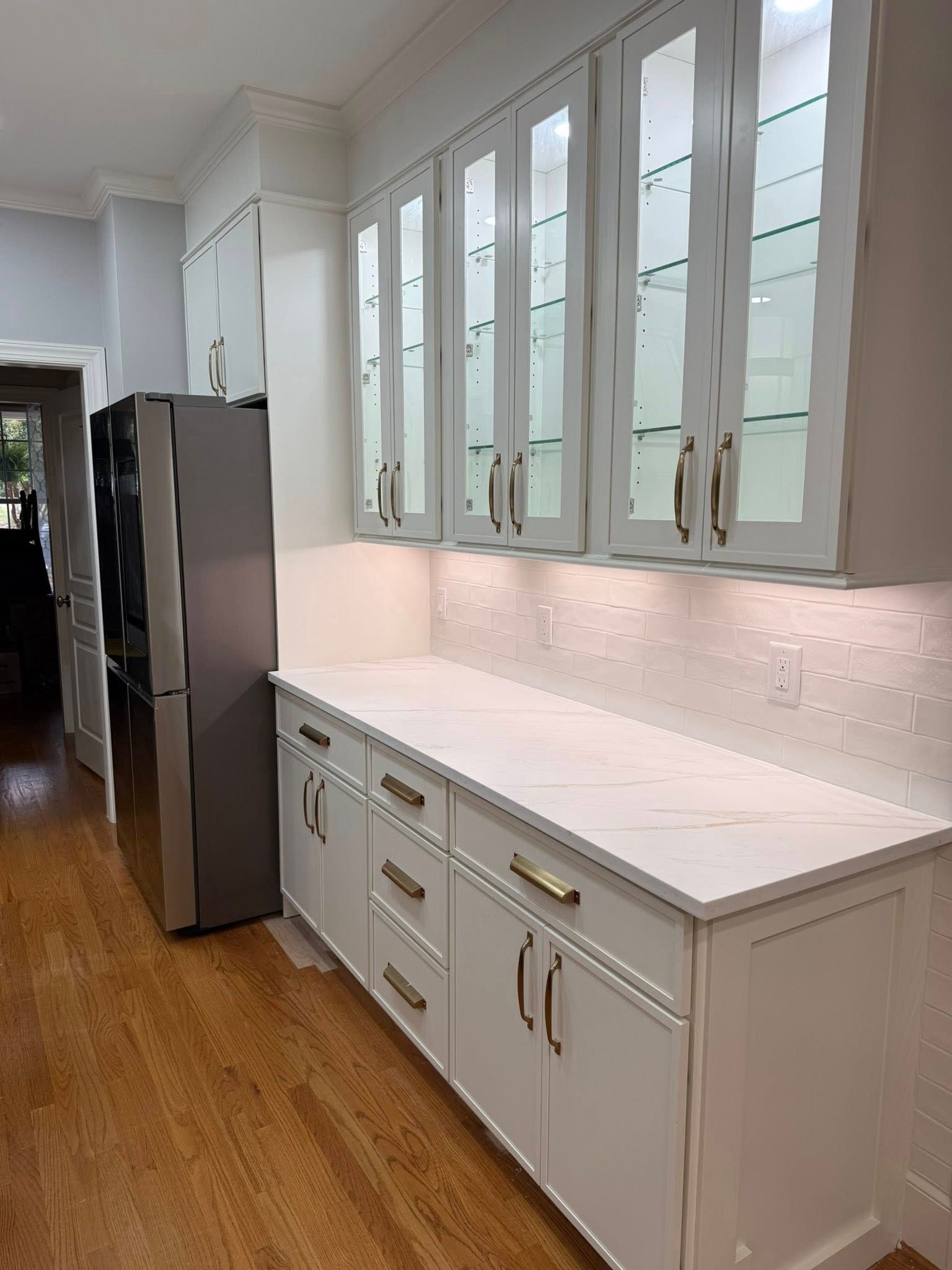 White kitchen cabinets with glass doors, white countertops, and stainless steel refrigerator.